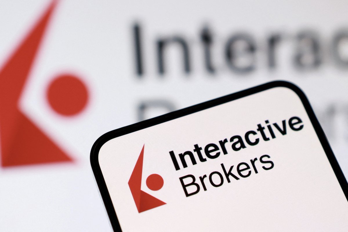 A smartphone screen displaying the Interactive Brokers logo in front of an out-of-focus background showing the same company logo.