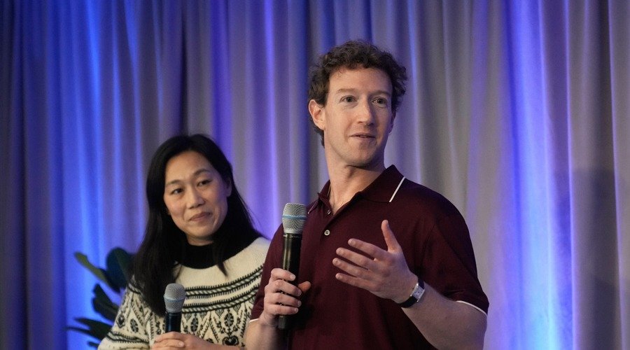 Mark Zuckerberg speaking into a microphone alongside Priscilla Chan against a blue curtain backdrop.