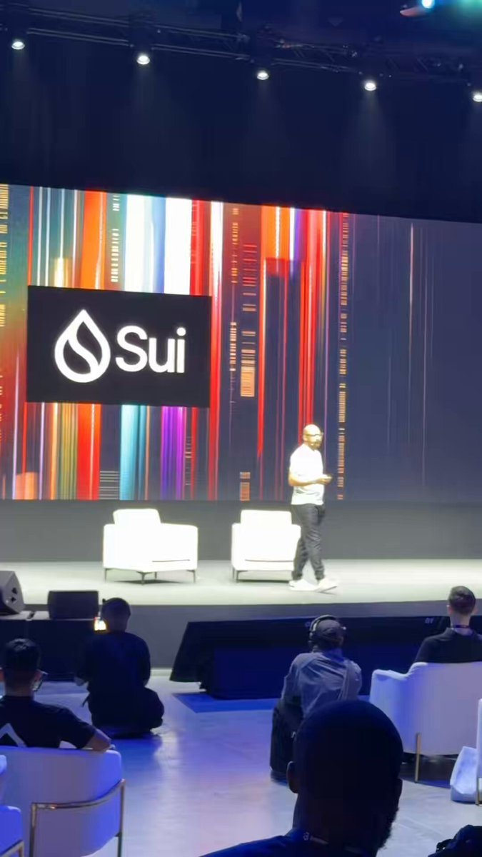 A presenter walks across an event stage in front of a screen displaying the Sui network logo.