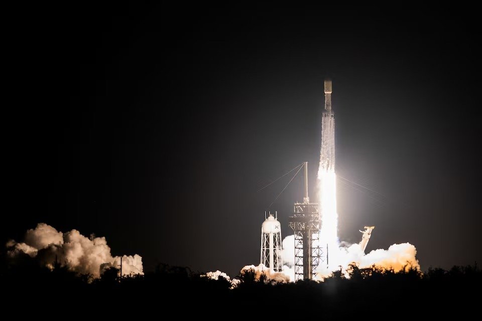 A SpaceX rocket lifts off from a launch pad illuminated by exhaust flames at night.