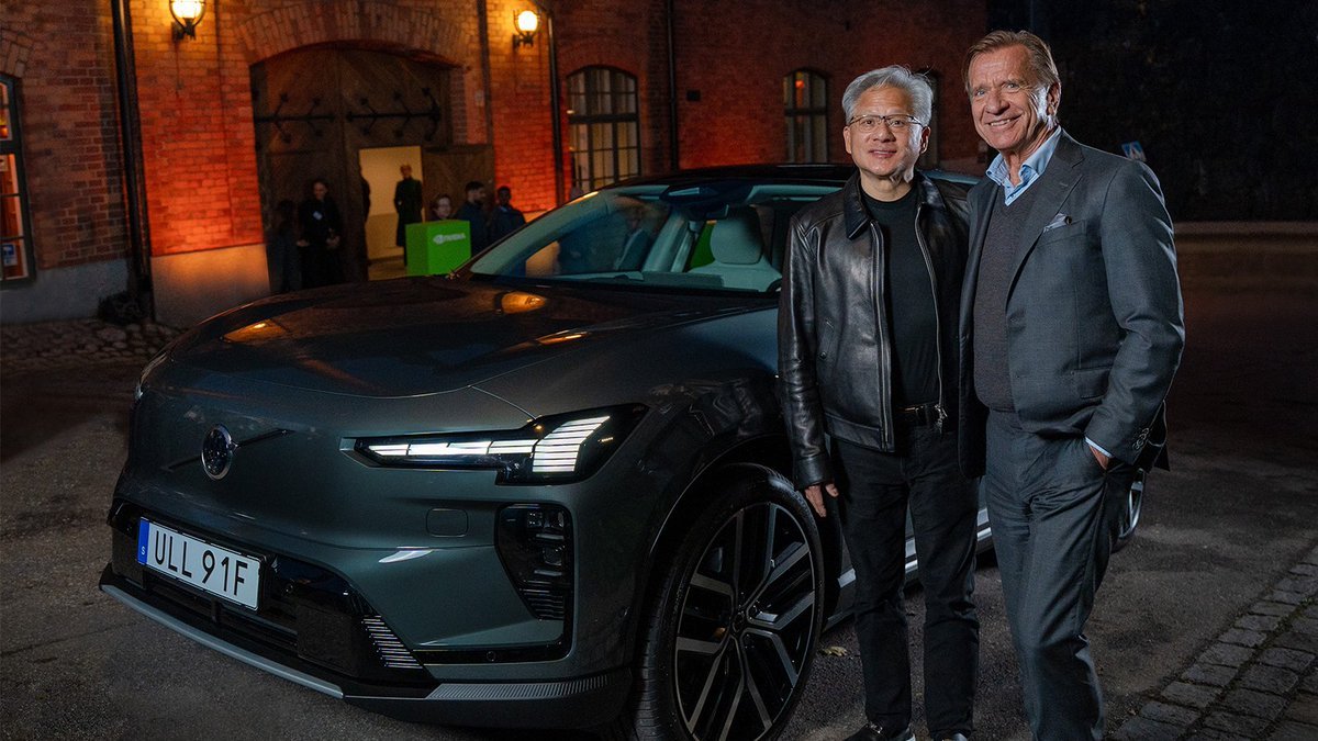 Nvidia CEO Jensen Huang and Volvo CEO Jim Rowan standing next to a Volvo vehicle at night.