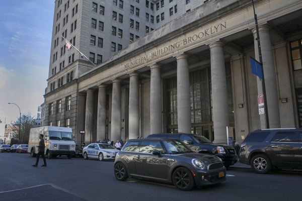Exterior view of the Brooklyn Municipal Building with parked cars and street traffic in front.