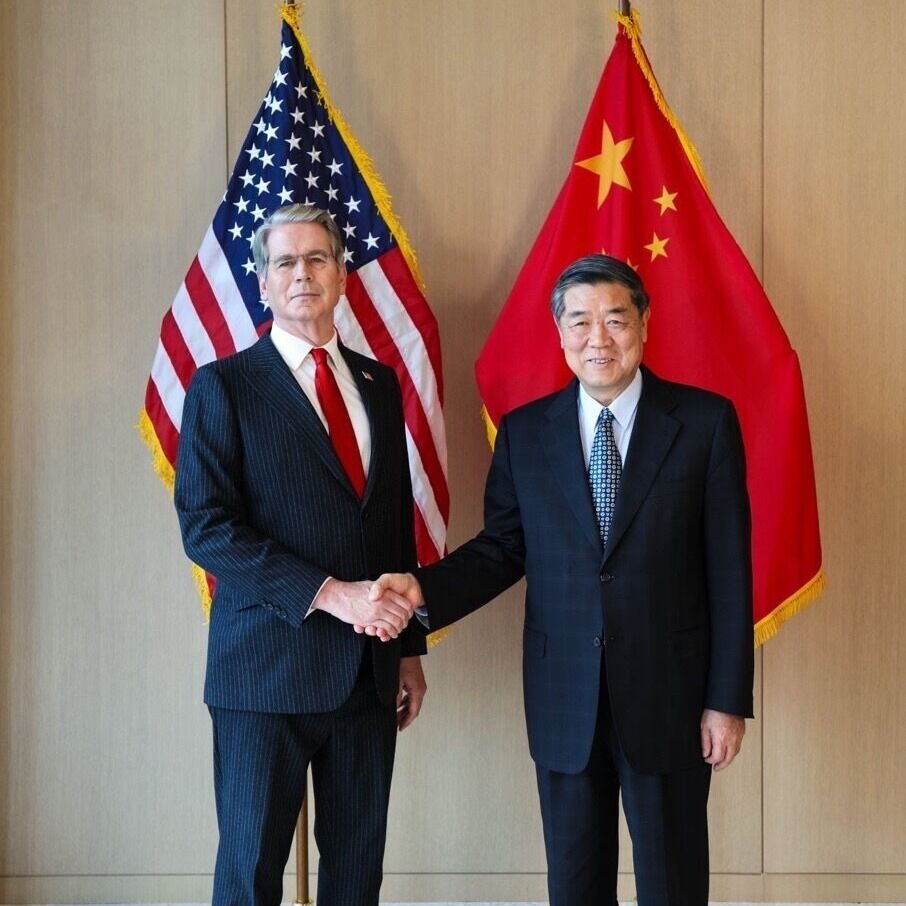 US Treasury Secretary Scott Bessent and Chinese Vice Premier He Lifeng shaking hands in front of the American and Chinese flags.