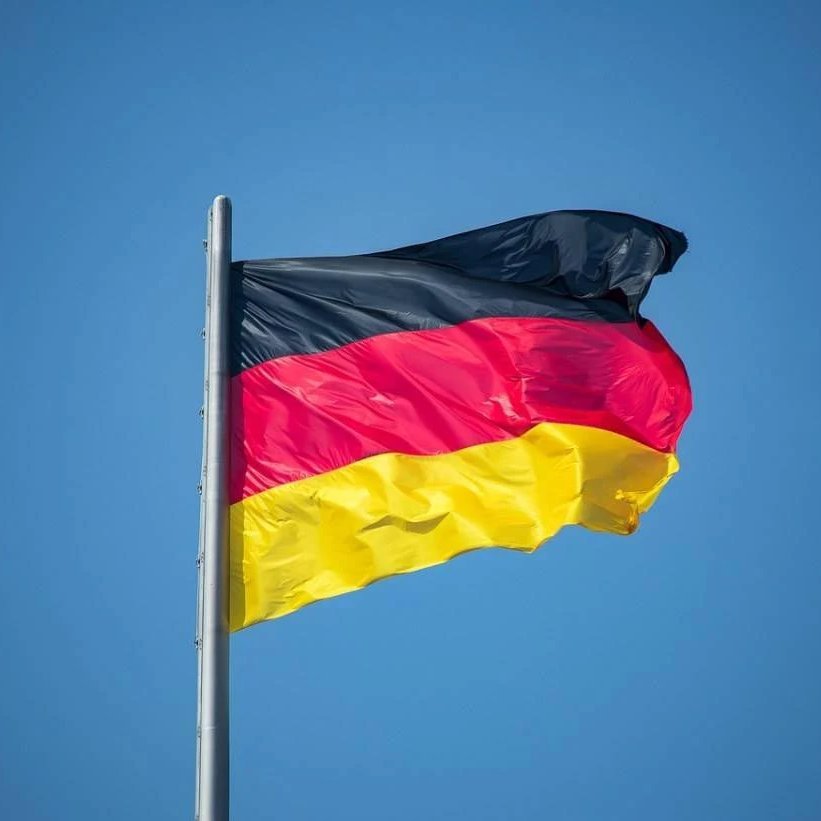 A German flag waving on a flagpole against a clear blue sky.