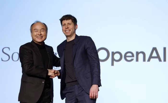 SoftBank CEO Masayoshi Son and OpenAI CEO Sam Altman shaking hands on stage in front of SoftBank and OpenAI logos.