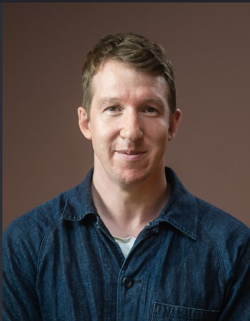 A portrait of Anthropic co-founder Jack Clark wearing a denim shirt against a neutral background.