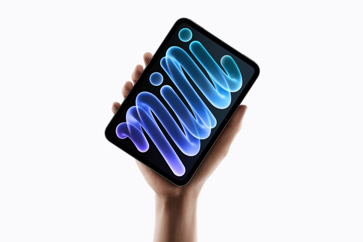 A hand holding the new Apple iPad mini displaying a blue abstract wallpaper against a white background.