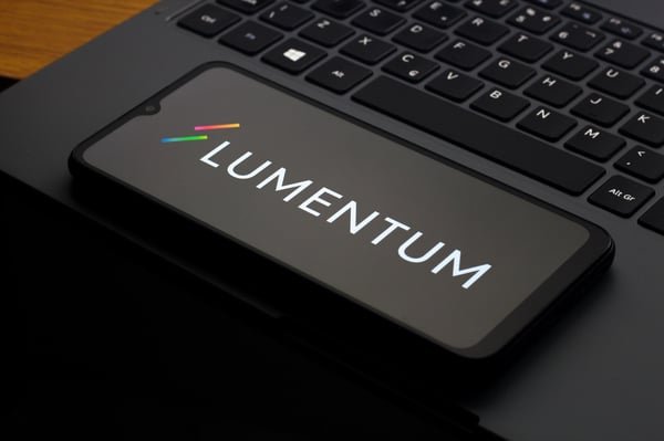 A smartphone displaying the Lumentum logo resting on a laptop keyboard.
