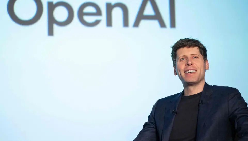 OpenAI CEO Sam Altman smiling on stage in front of an OpenAI logo