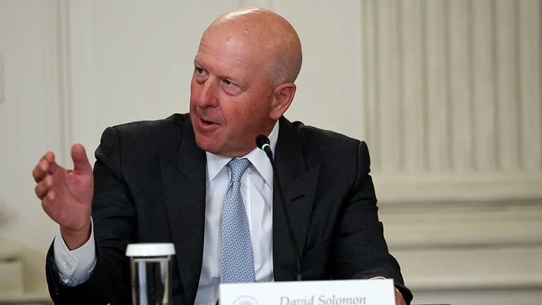 Goldman Sachs CEO David Solomon speaking at a panel discussion with a microphone and nametag.