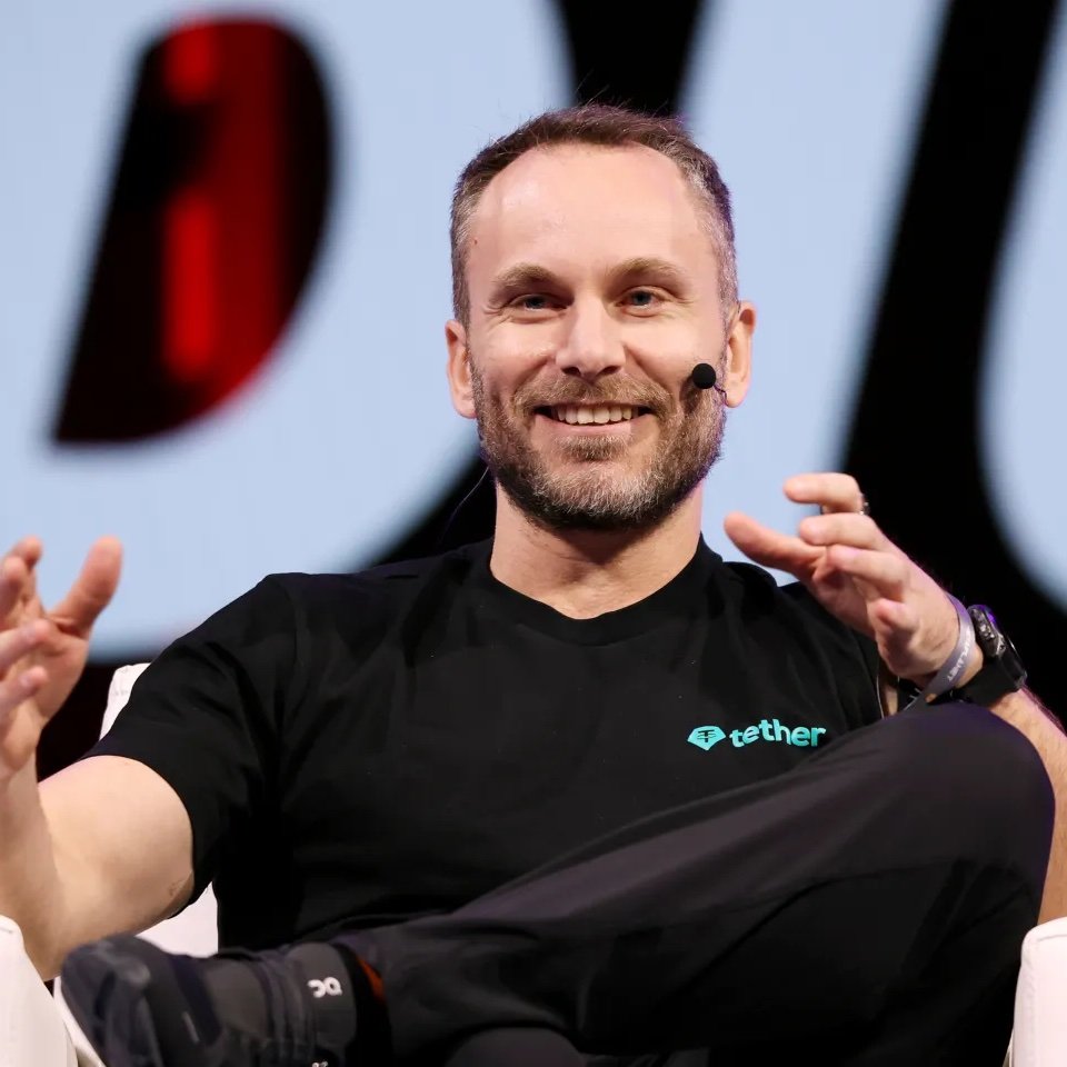 Paolo Ardoino speaking at a conference while wearing a black Tether t-shirt.