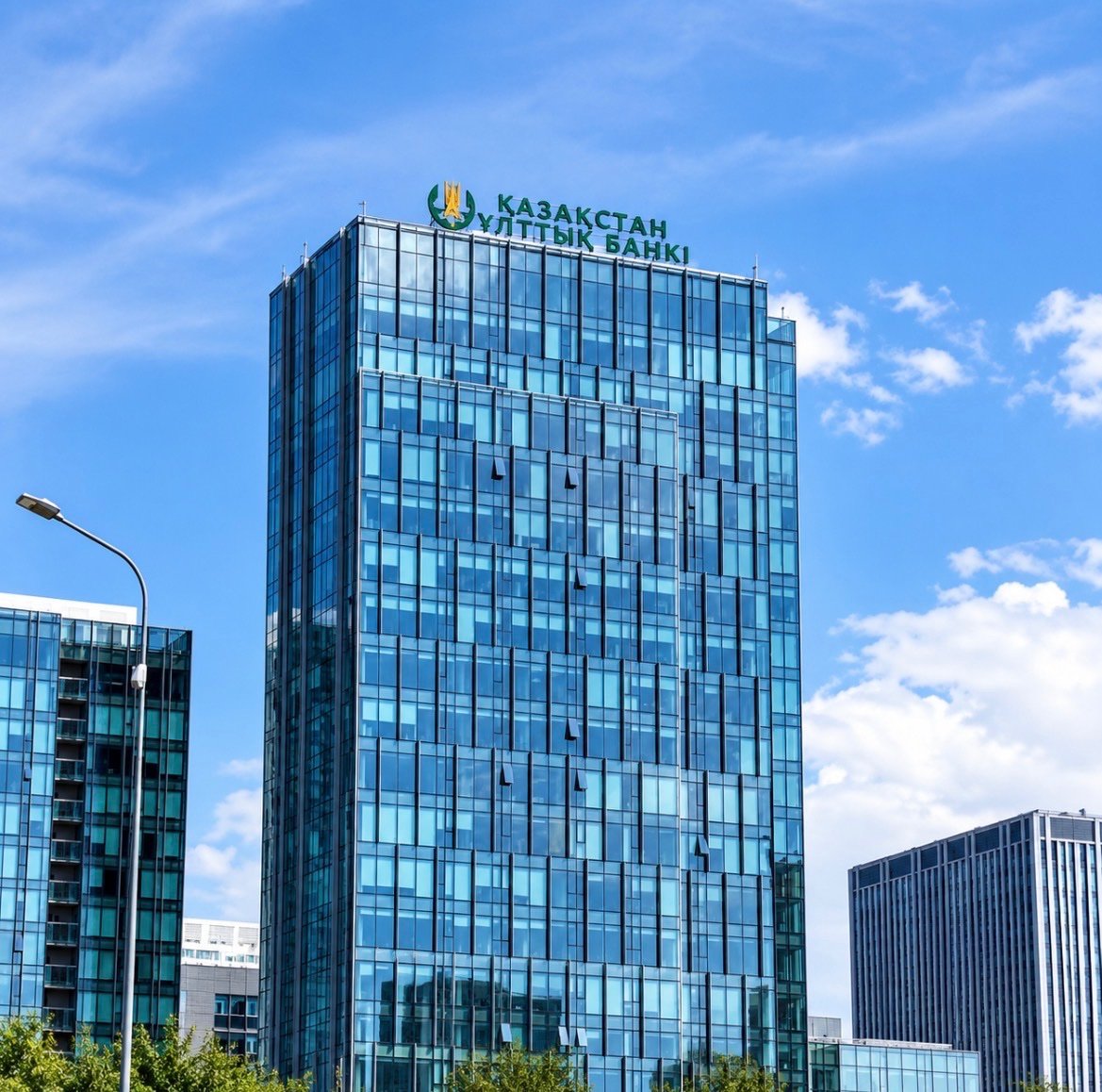 A glass high-rise building with the National Bank of Kazakhstan logo and text at the top against a blue sky.