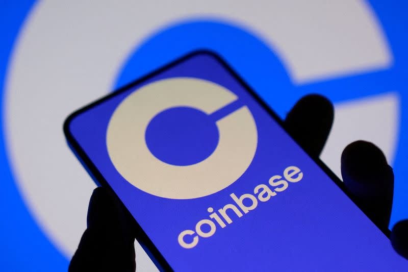 A smartphone displaying the Coinbase logo held against a blue background.