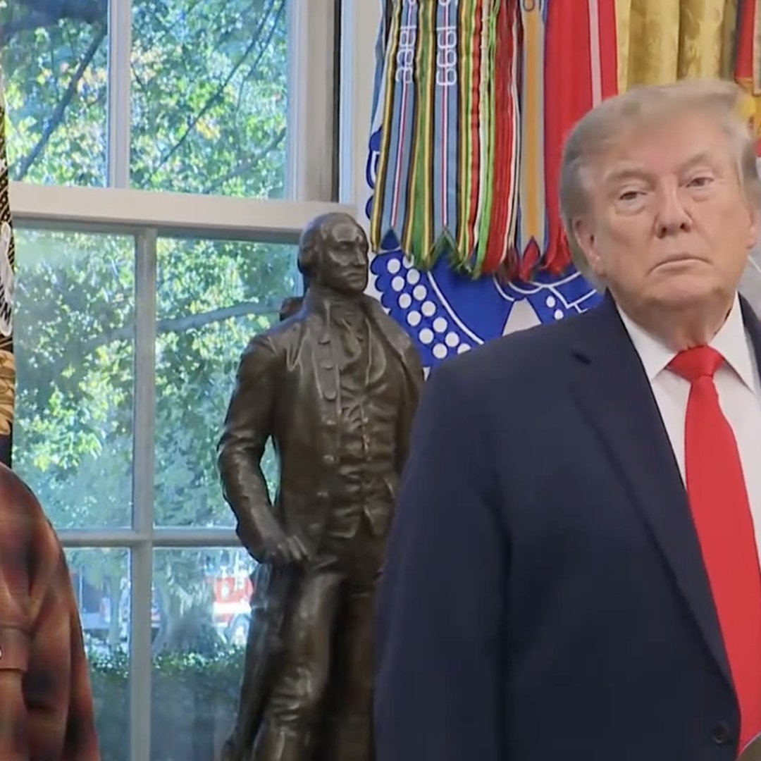 Donald Trump in a suit and red tie during a White House event, standing near a bronze statue of George Washington.