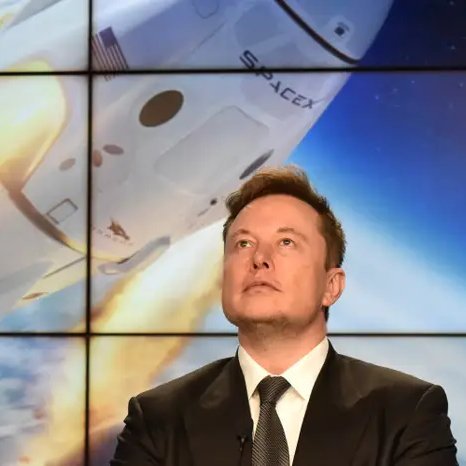 SpaceX founder Elon Musk looking upward in front of a screen displaying a SpaceX spacecraft