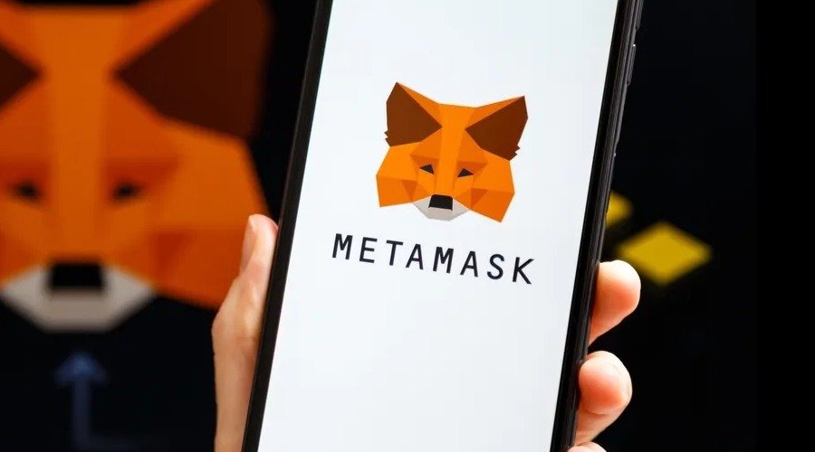 A hand holding a smartphone displaying the orange MetaMask fox logo and brand name on its screen.