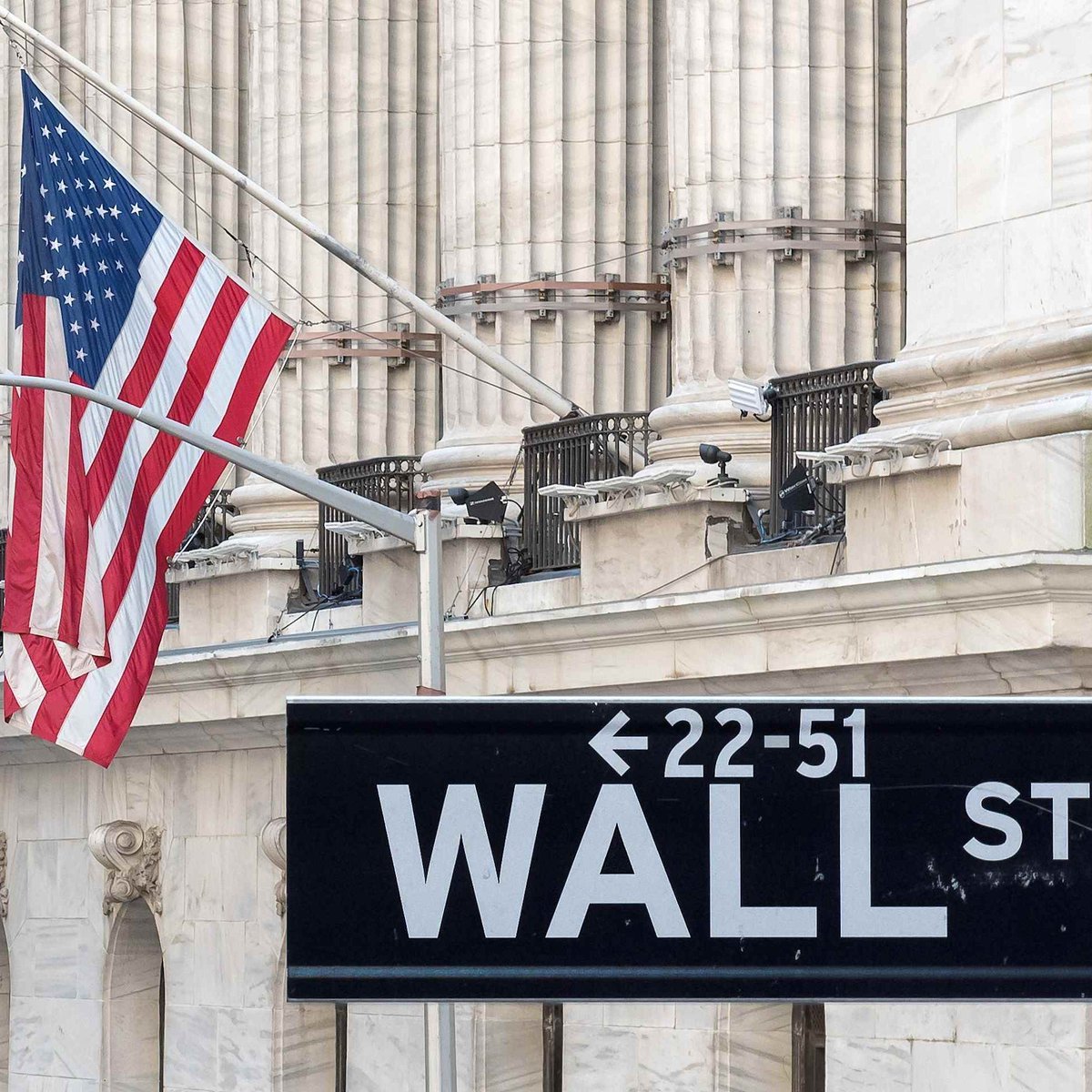 A Wall Street sign mounted on a post in front of a classical stone building facade with an American flag.