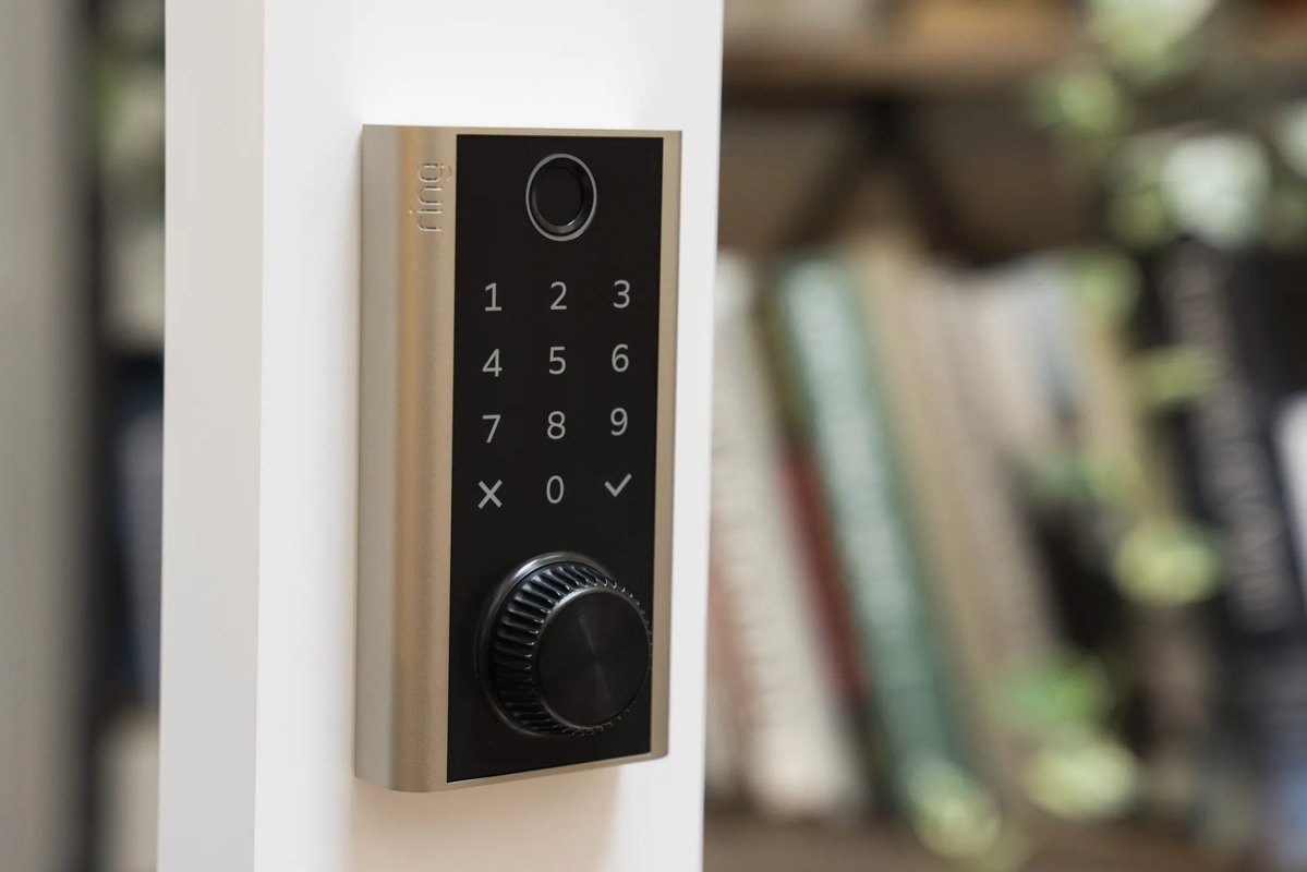 Ring smart lock installed on a door frame, featuring a numeric keypad, fingerprint scanner, and manual power dial at the bottom.