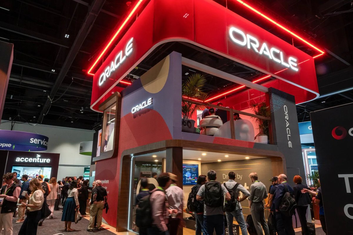 An Oracle exhibition pavilion with illuminated signage and attendees gathered on a conference floor.