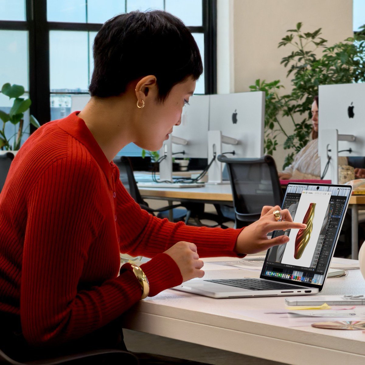 A person seated at an office desk touches the screen of the newly unveiled MacBook Pro laptop while working in a graphics editing application.