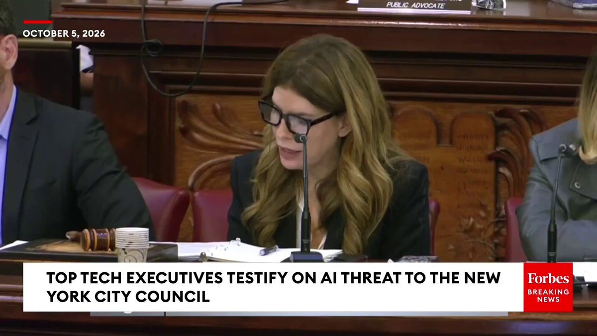 A woman speaking at a microphone during a New York City Council hearing titled 'Top Tech Executives Testify on AI Threat to the New York City Council'.