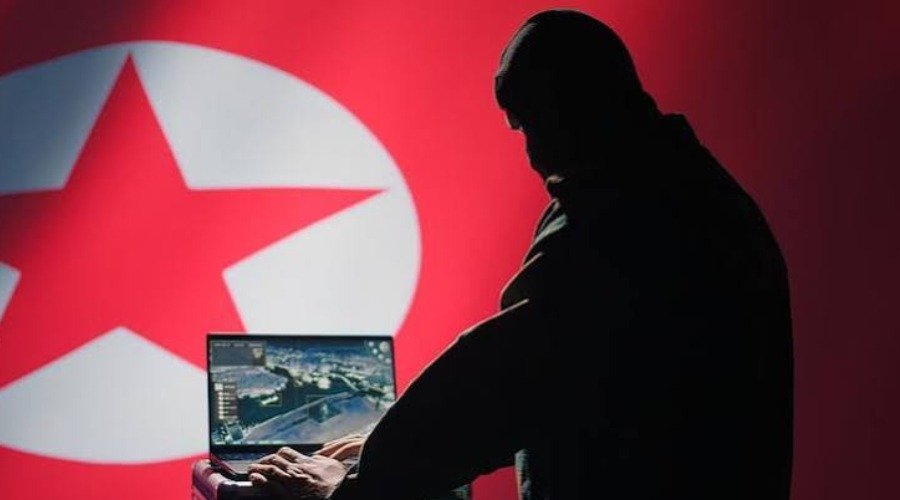 An illustrative silhouette of a person using a laptop computer against the background of the North Korean flag.