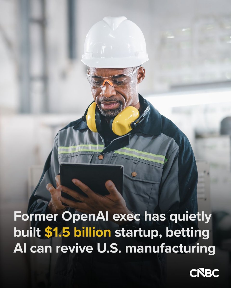 A factory engineer wearing a hard hat, protective goggles, and ear protection looks down at a digital tablet.
