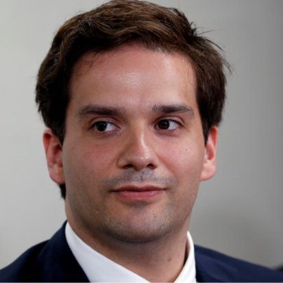 Close-up portrait of Mark Karpelès looking slightly to the side in a suit and white collared shirt.