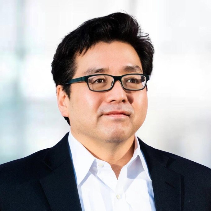 Portrait of BitMine Chairman Tom Lee wearing glasses, a white collared shirt, and a dark suit jacket.
