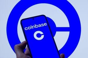 A smartphone displaying the Coinbase logo held against a screen showing the Coinbase emblem.