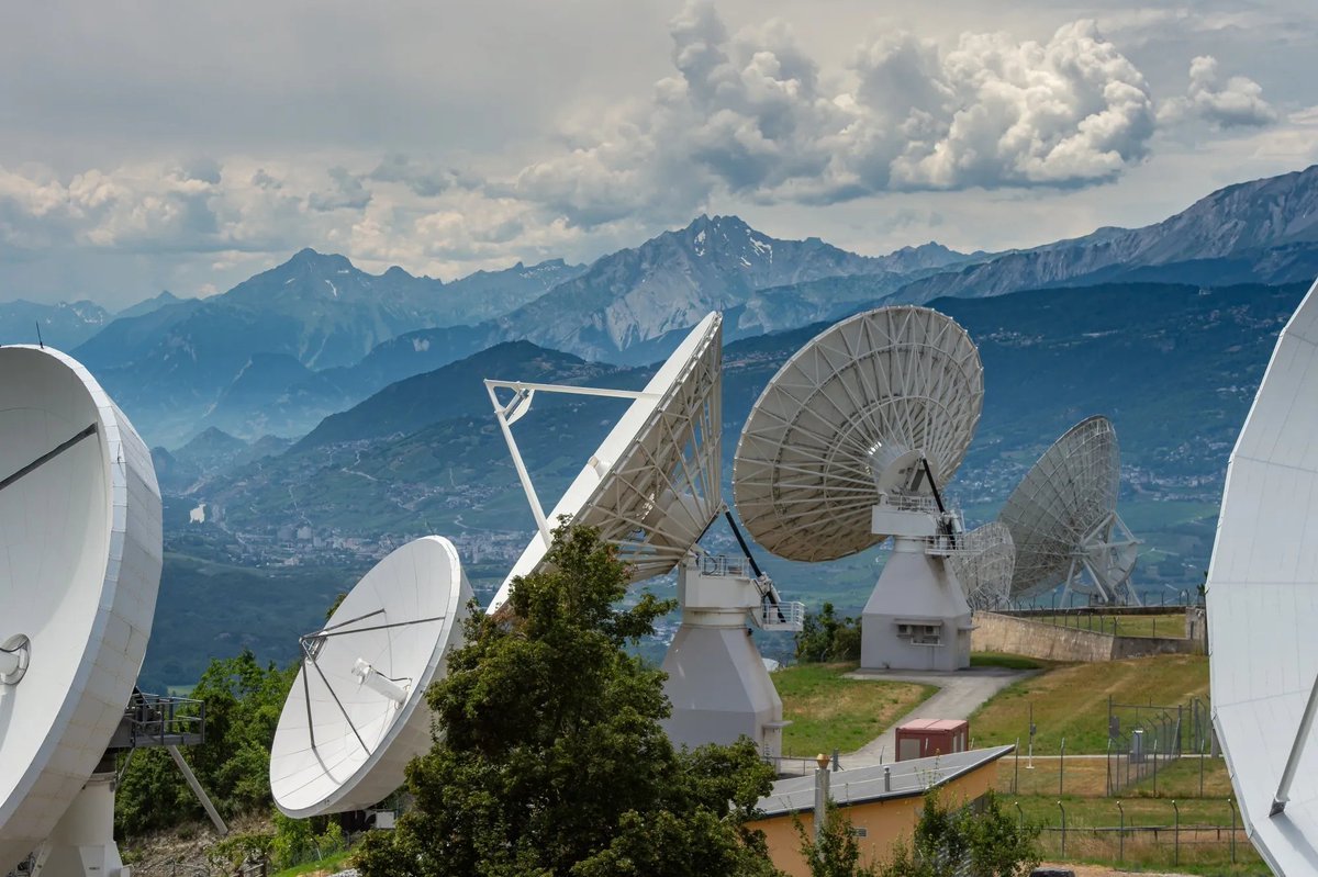 Satellite dish antennas at a ground communication station with mountains in the background.