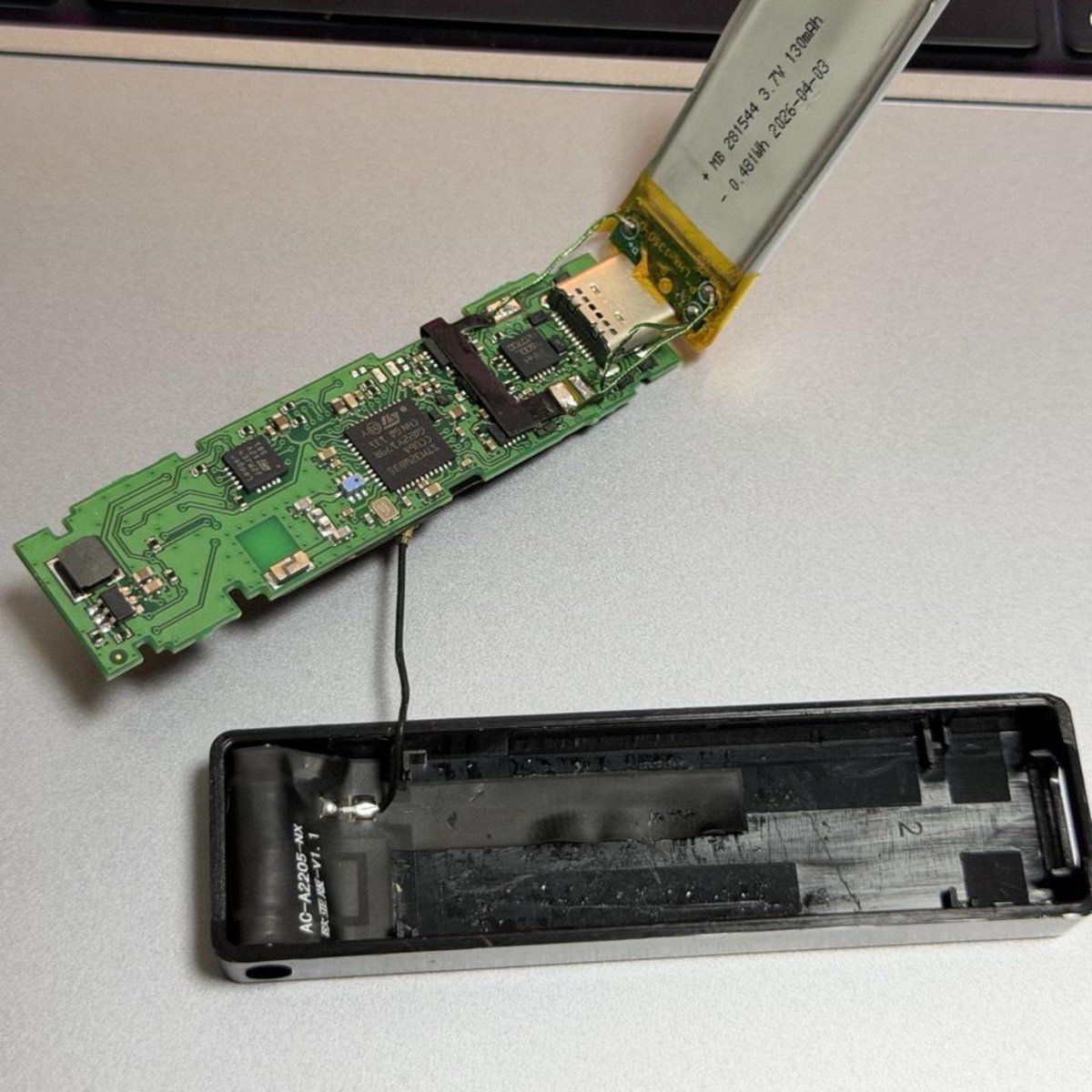 Disassembled Ledger Nano X hardware wallet showing an internal circuit board connected via thin wiring to an antenna in the case and an attached battery.