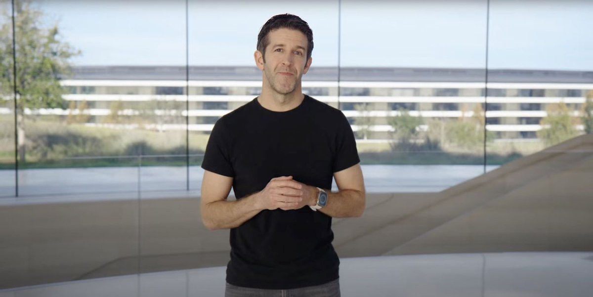 Apple CEO John Ternus standing indoors with Apple Park visible through large glass windows behind him.