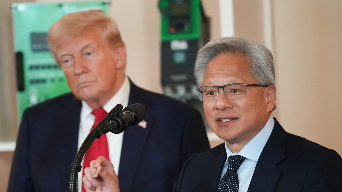 Donald Trump stands in the background as Nvidia CEO Jensen Huang speaks at a microphone.