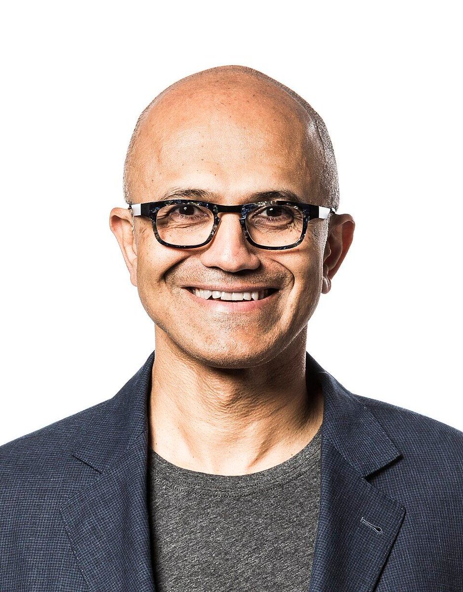 Portrait photo of Microsoft CEO Satya Nadella smiling with glasses against a white background.
