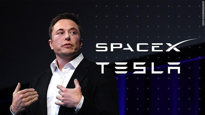 Elon Musk gesturing on stage beside the SpaceX and Tesla logos.