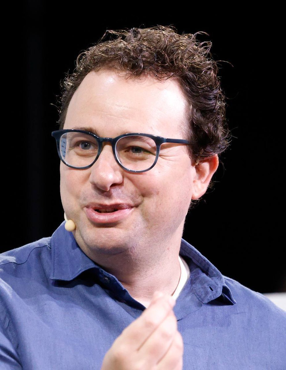 Anthropic co-founder and CEO Dario Amodei speaking on stage wearing glasses and a blue shirt.