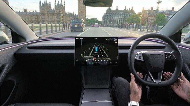 View from inside a Tesla car showing the steering wheel and center touchscreen display operating driver-assistance software while driving across a bridge.
