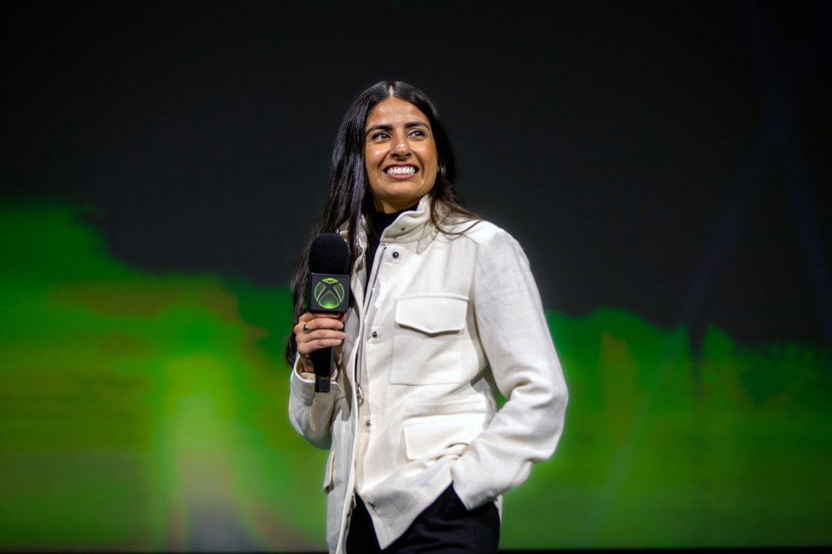 Asha Sharma speaking on stage holding an Xbox microphone.
