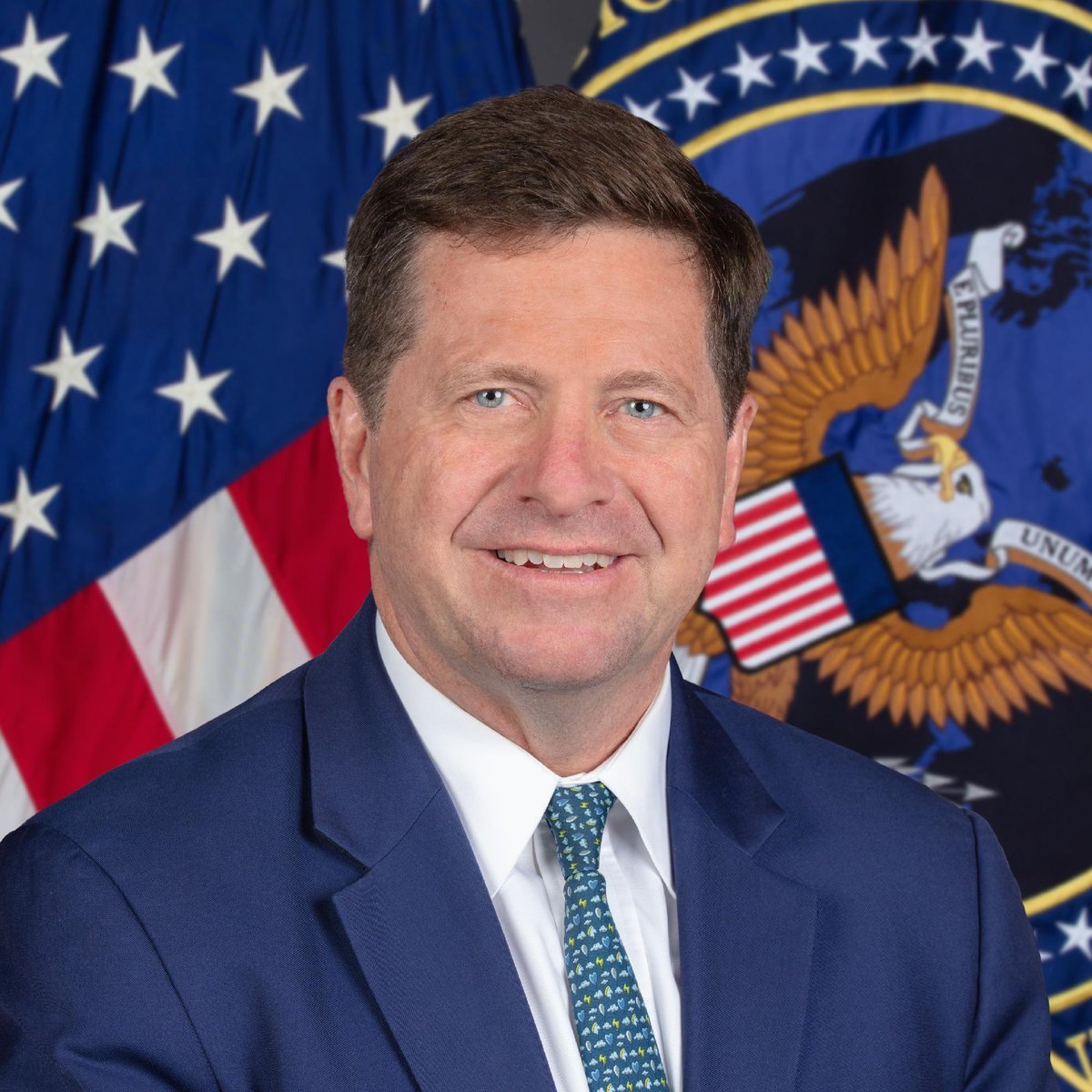 Official portrait of Jay Clayton in a blue suit with American flags in the background.