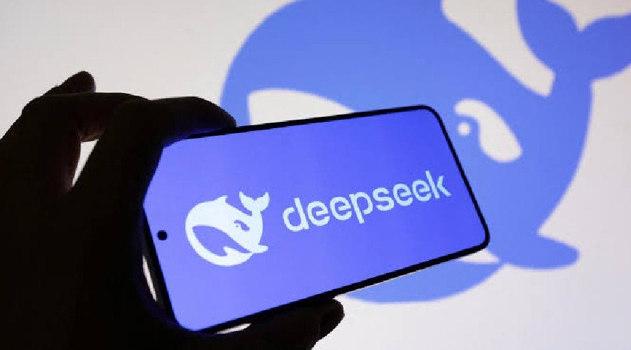 A hand holding a smartphone displaying the DeepSeek logo in front of a backlit DeepSeek whale symbol.
