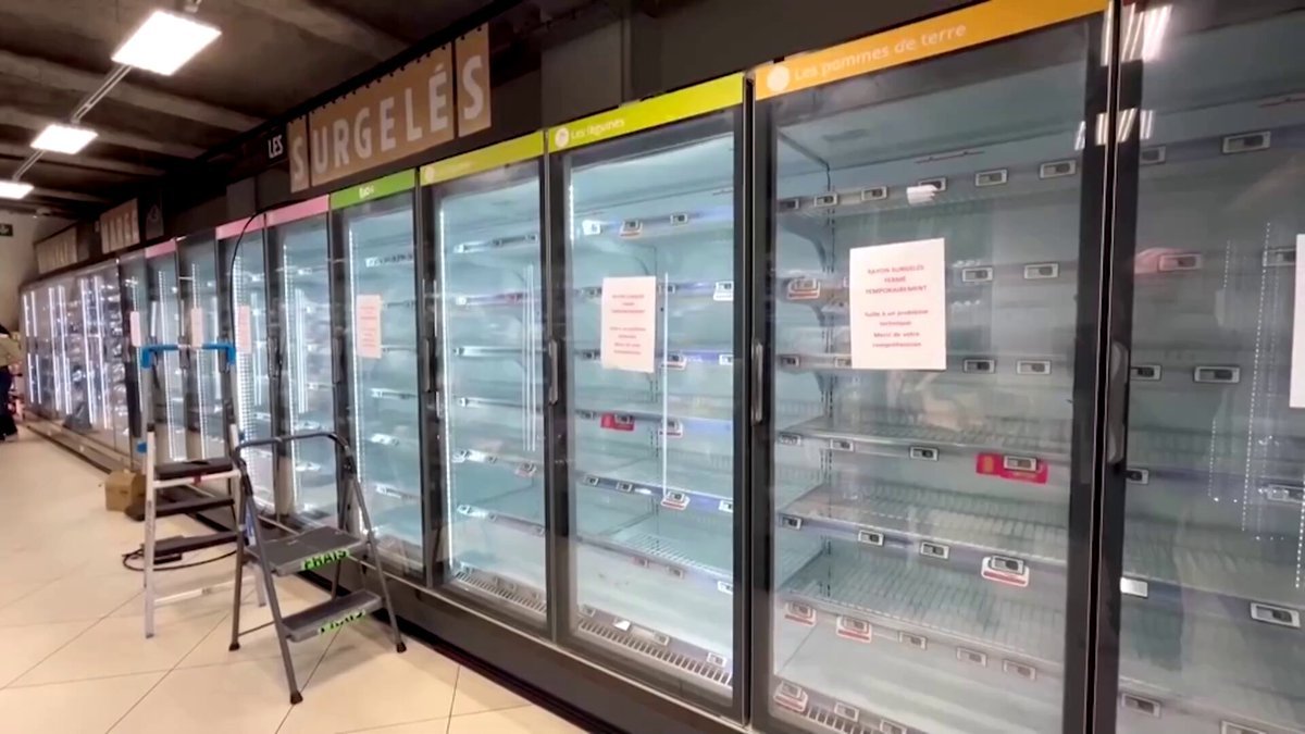 Empty refrigerated display cases line an aisle in a French supermarket with advisory notices posted on the glass doors.