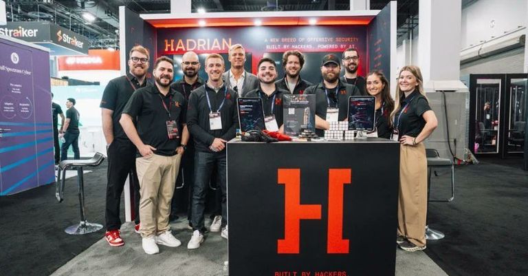 Members of the Hadrian team standing together at a conference exhibition booth featuring the Hadrian logo and branding.
