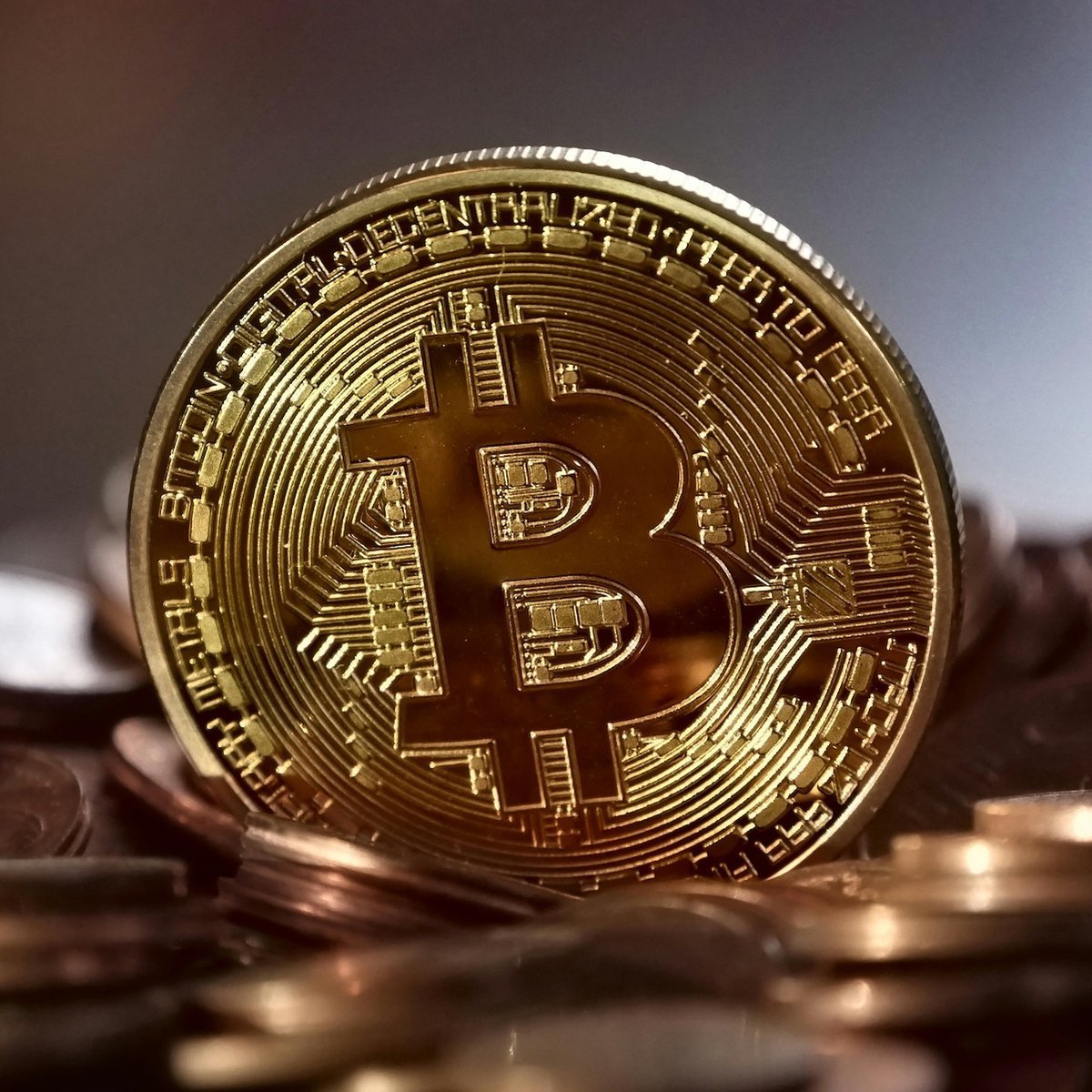 A shiny physical gold Bitcoin token resting on a stack of coins.