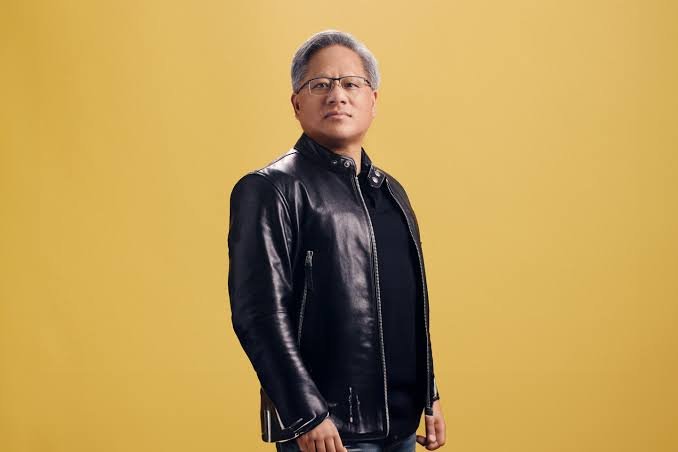 Portrait of Nvidia CEO Jensen Huang wearing glasses and a black leather jacket against a yellow background.