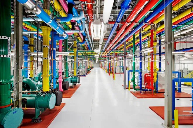 Interior view of a Google data center showing colorful pipes running along the ceiling and floor.