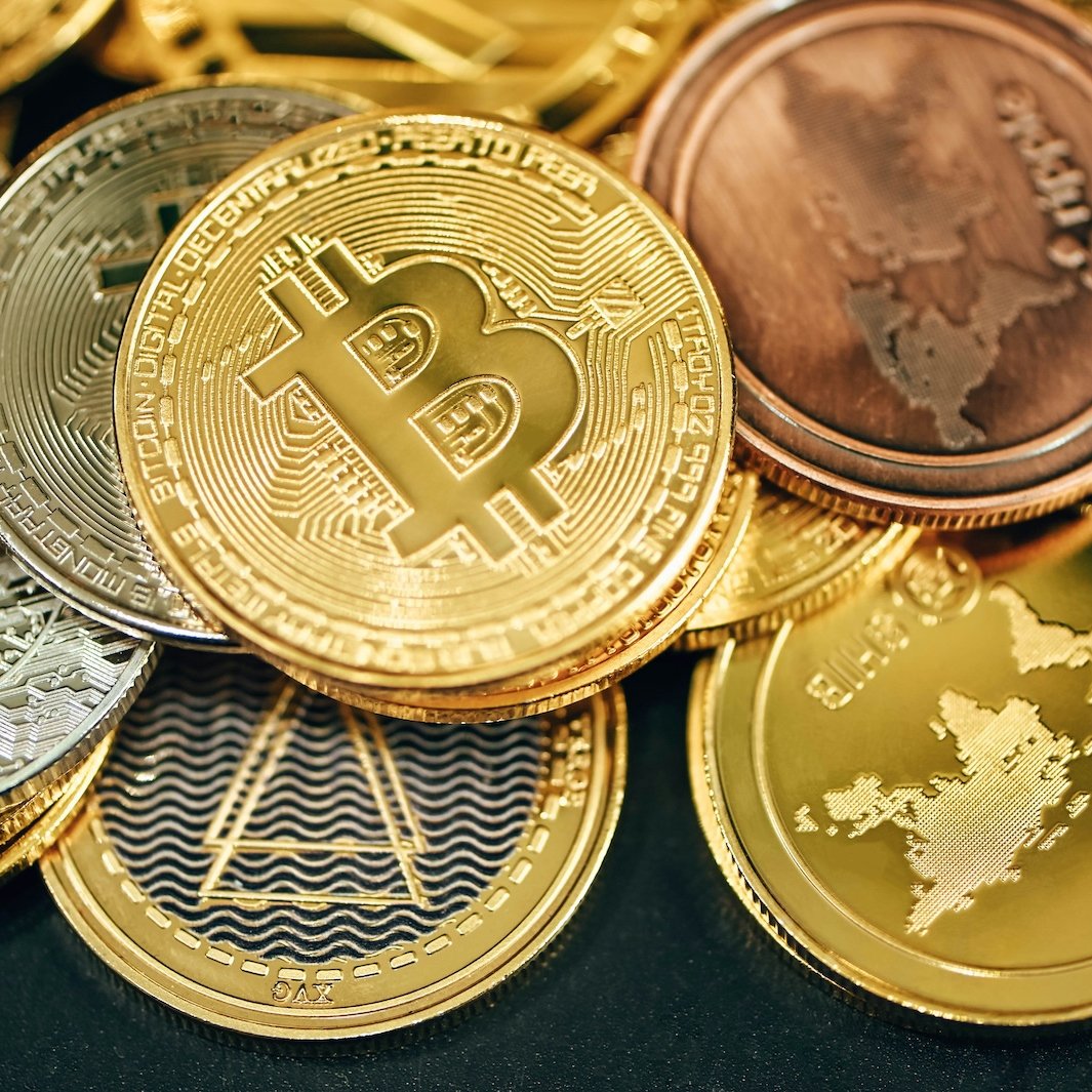 Physical commemorative coins representing Bitcoin and other cryptocurrencies stacked together.