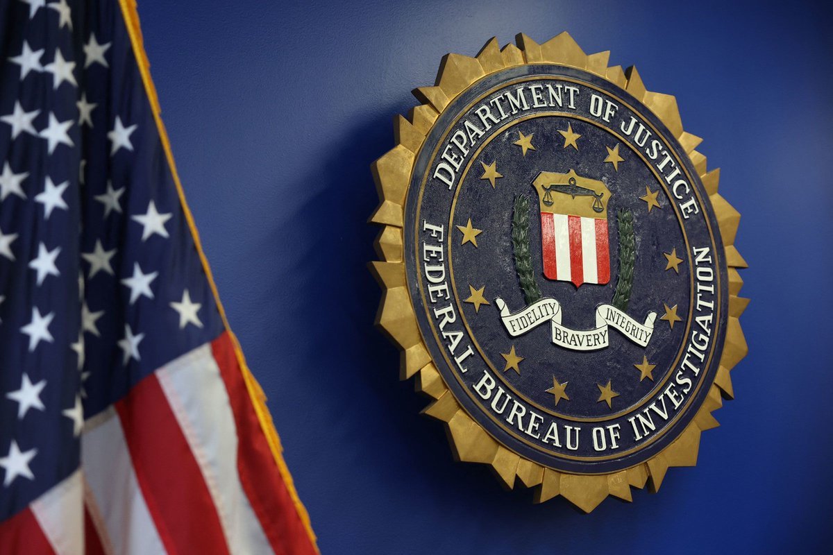 An FBI seal mounted on a blue wall next to an American flag.