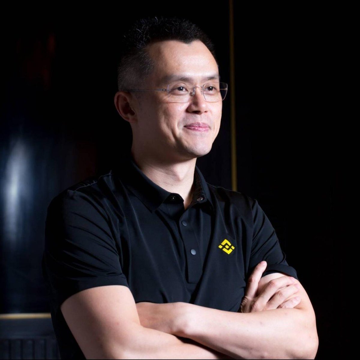 Portrait of Binance founder Changpeng Zhao wearing glasses and a black polo shirt with his arms crossed.